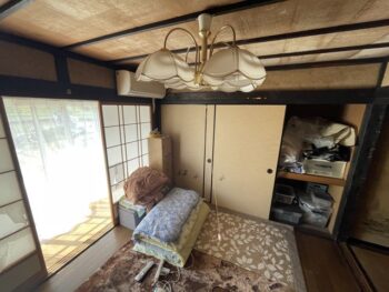 リフォーム前の和室。シャンデリア風照明・押入れの中に布団・こたつ・雑然とした収納など、経年感のある空間