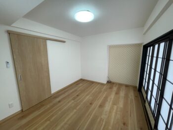 リフォーム後の洋室。明るい無垢調フローリング・木目調の引き戸・市松模様のアクセントクロス・シーリングライト
