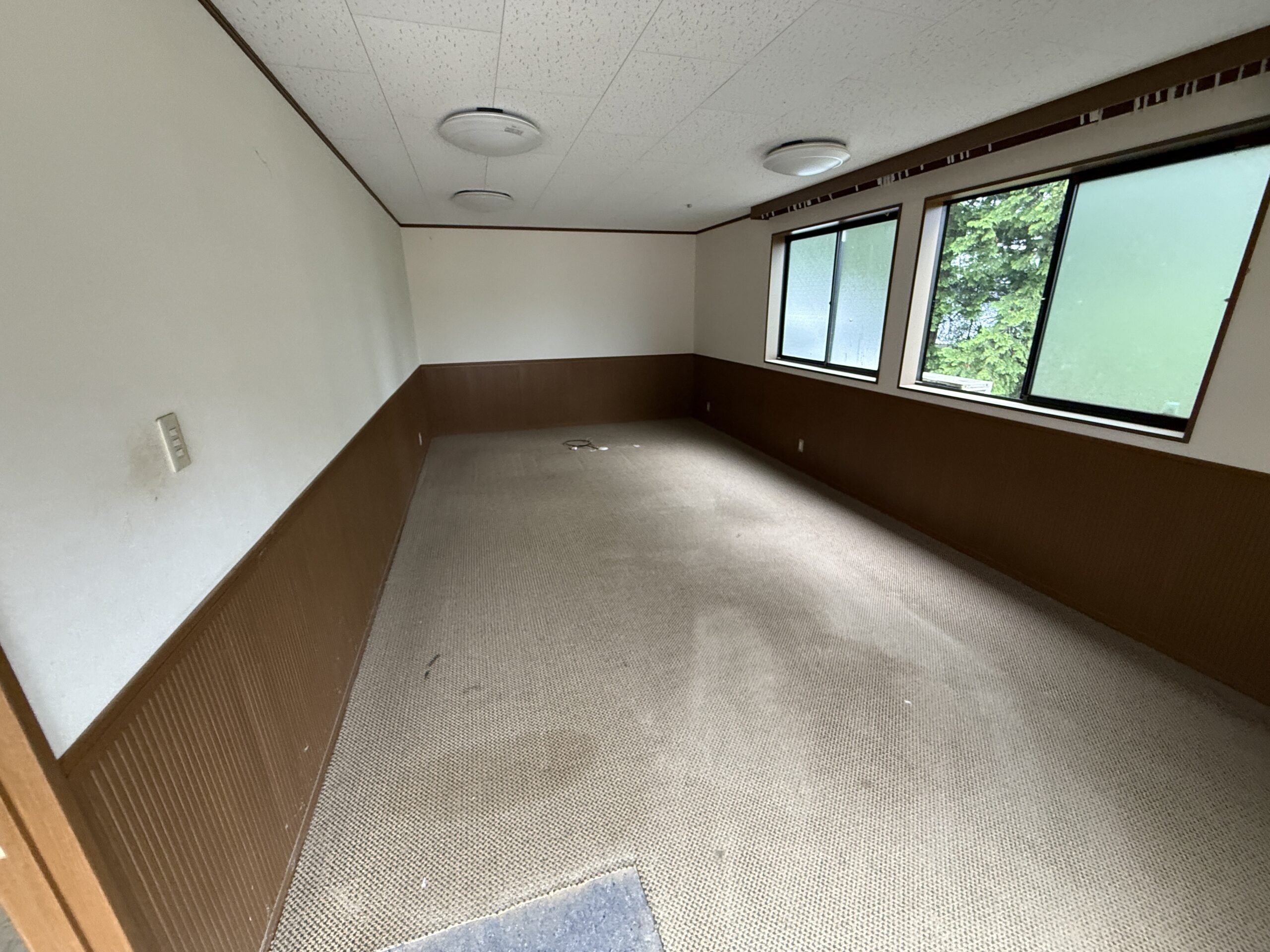 リフォーム前の既存居室。白い壁と茶色い木目腰壁、古い薄茶色カーペットで暗く古めかしい印象